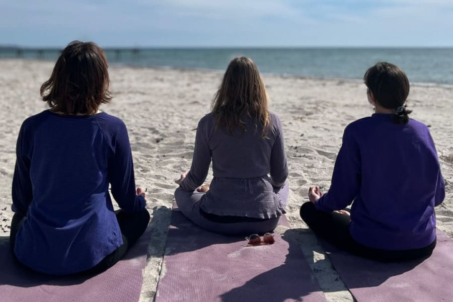 Woman meditating peacefully on the beach during sunrise at yog living retreat center in Sweden.