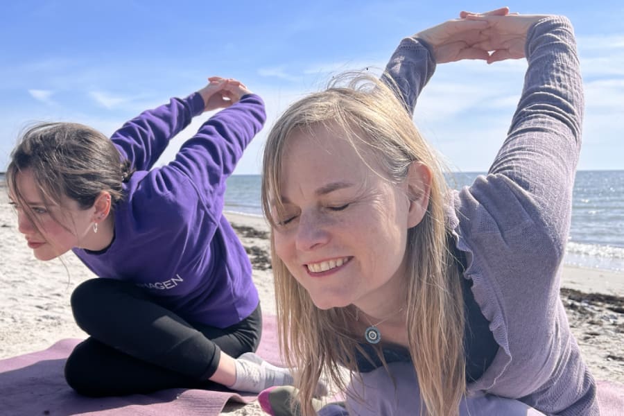 Happy women practicing shoelace pose during a prana yoga retreat on a beach in Sweden.
